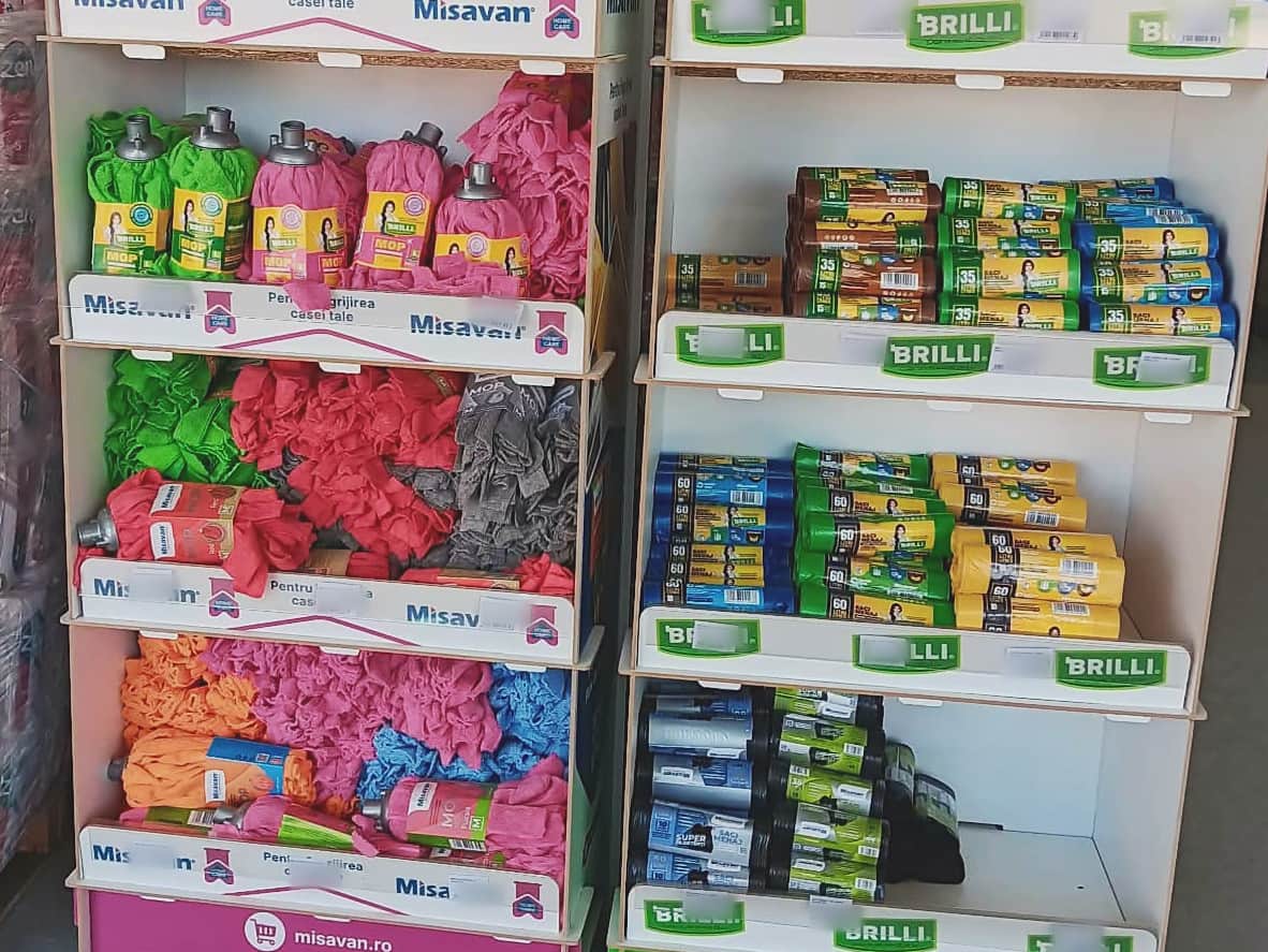 Standuri cu mopuri colorate, lavete și role de saci menajeri