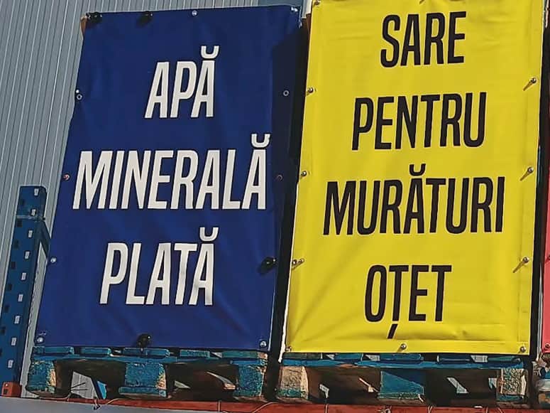 Bannere pe fațada depozitului: „Apă minerală plată” pe albastru și „Sare pentru murături, oțet” pe galben